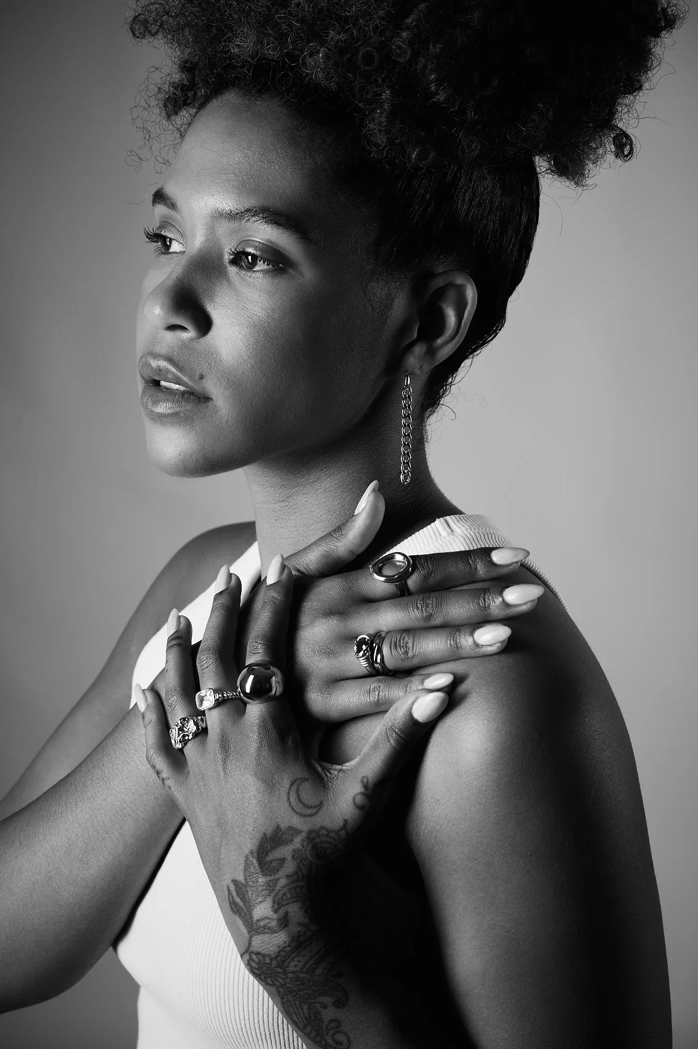 Woman wearing multiple statement rings and a chain earring, posing in black and white
