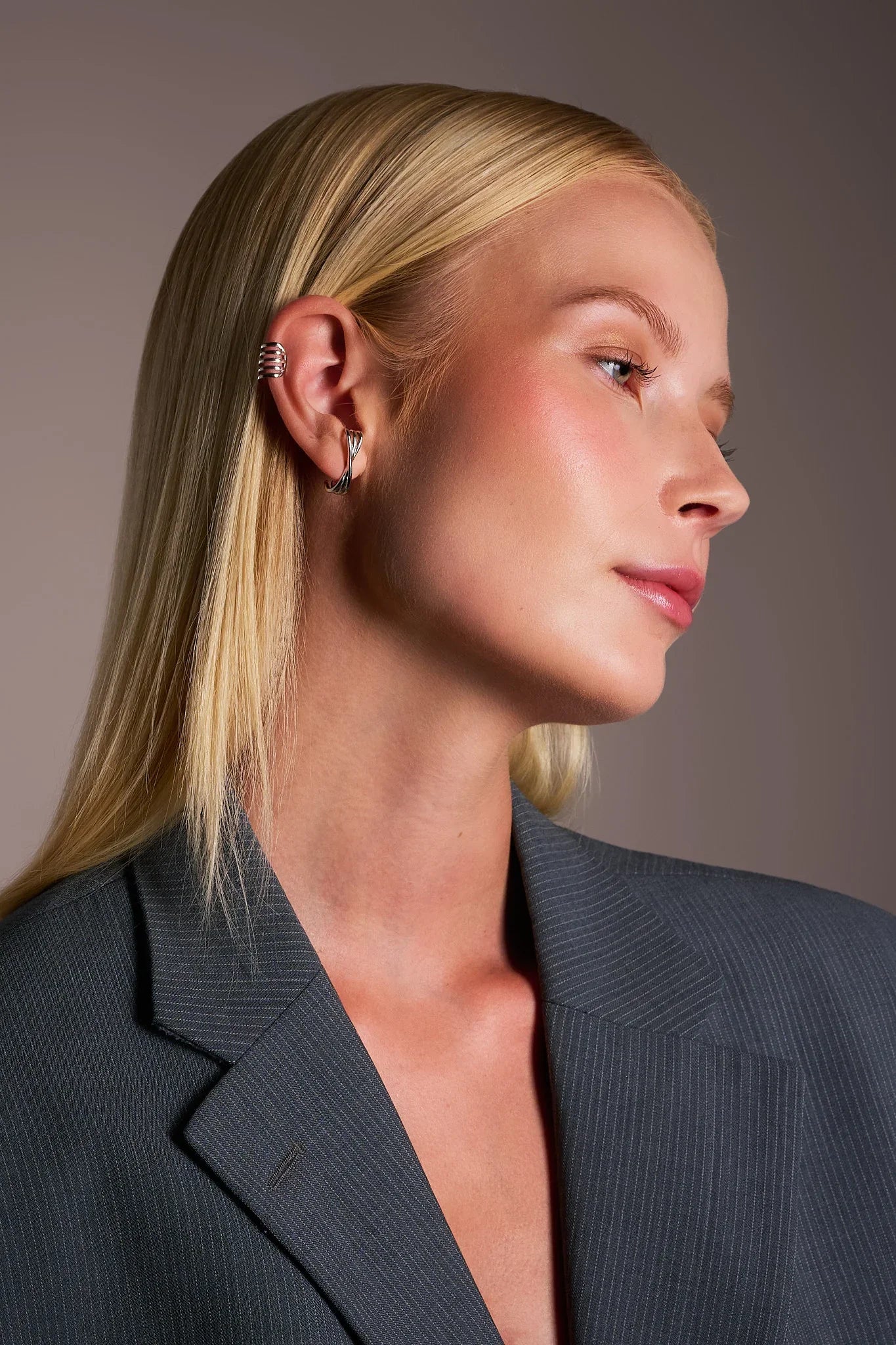 Woman wearing silver ear cuff and hoop earring with a pinstripe blazer