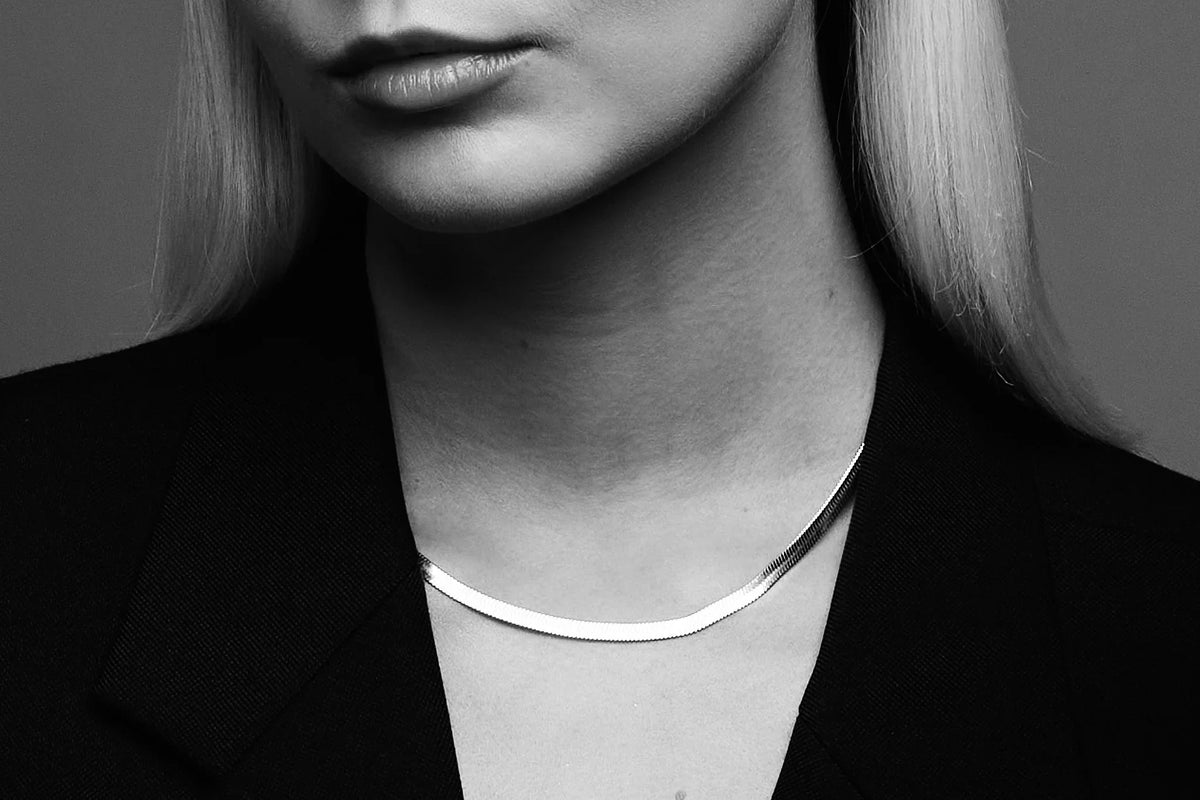 Woman wearing minimalist silver necklace with blazer, close-up, black and white