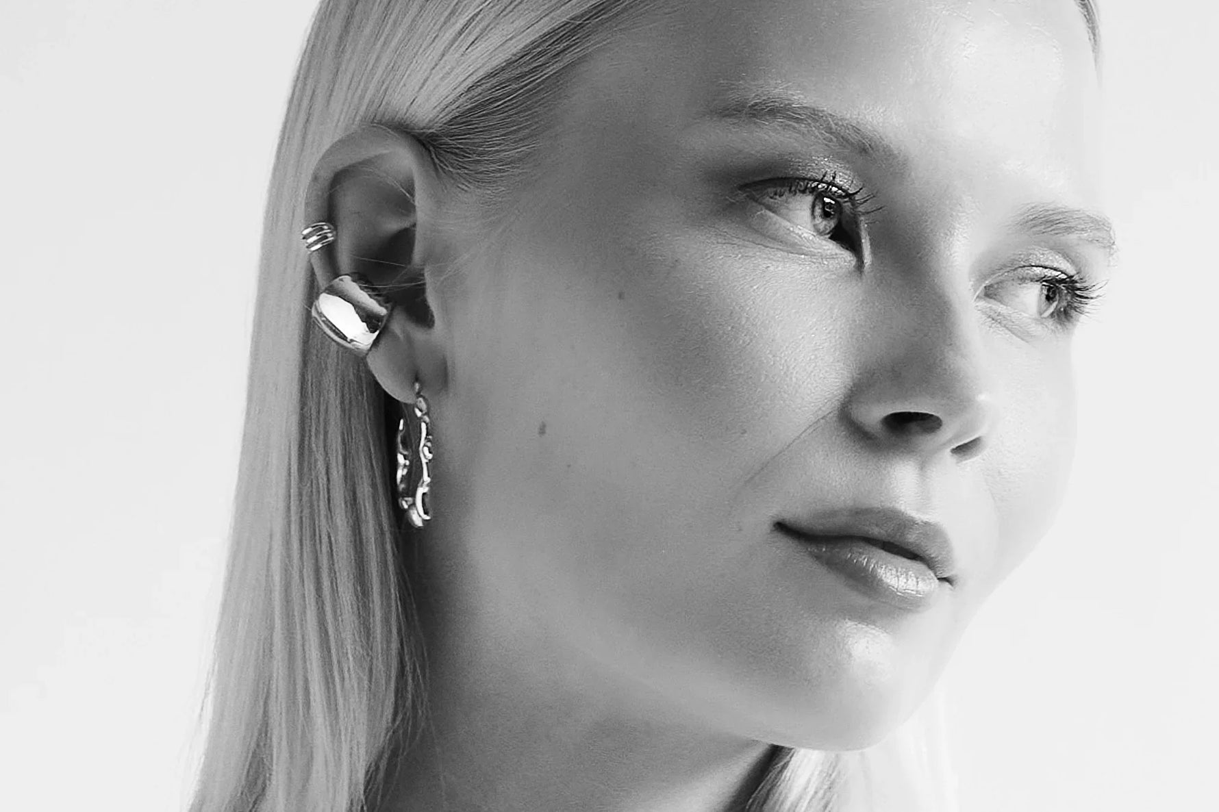 Woman wearing silver ear cuff and hoop earring, minimalist jewelry close-up