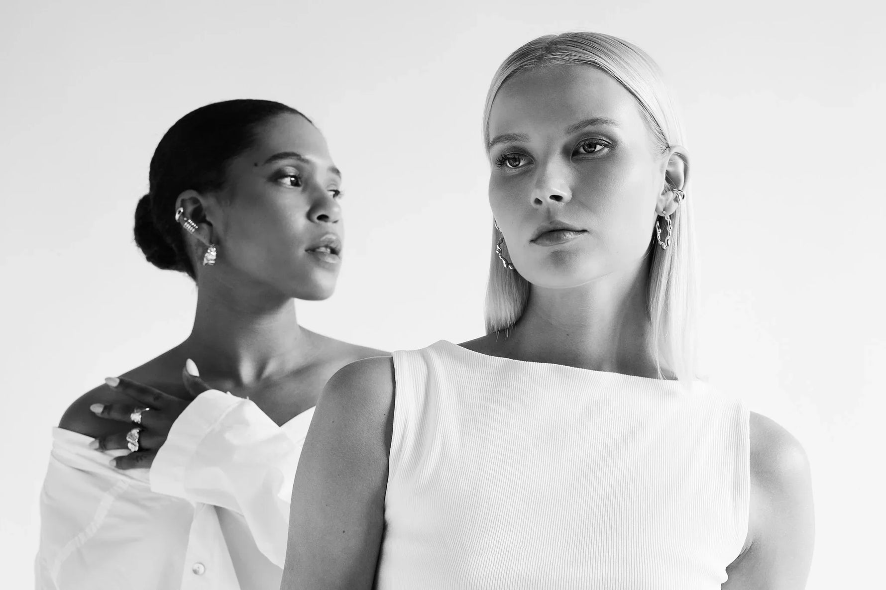 Two women showcasing modern silver earrings and rings in a minimalist setting