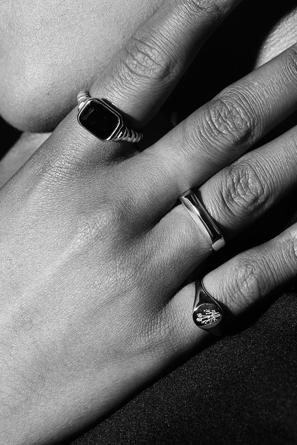 Close-up of hand wearing three unique silver rings, including a black gemstone and engraved design.