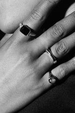 Close-up of hand wearing three silver rings, including a signet ring and black stone ring