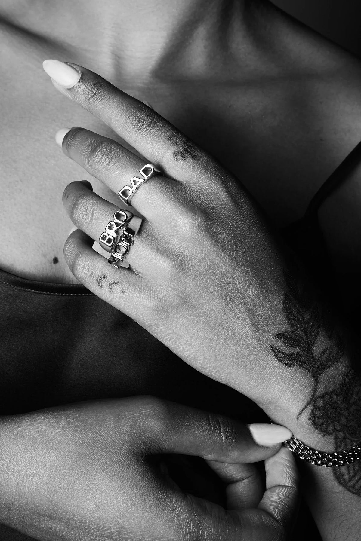 Close-up of hands wearing bold silver rings with engraved letters and floral tattoo