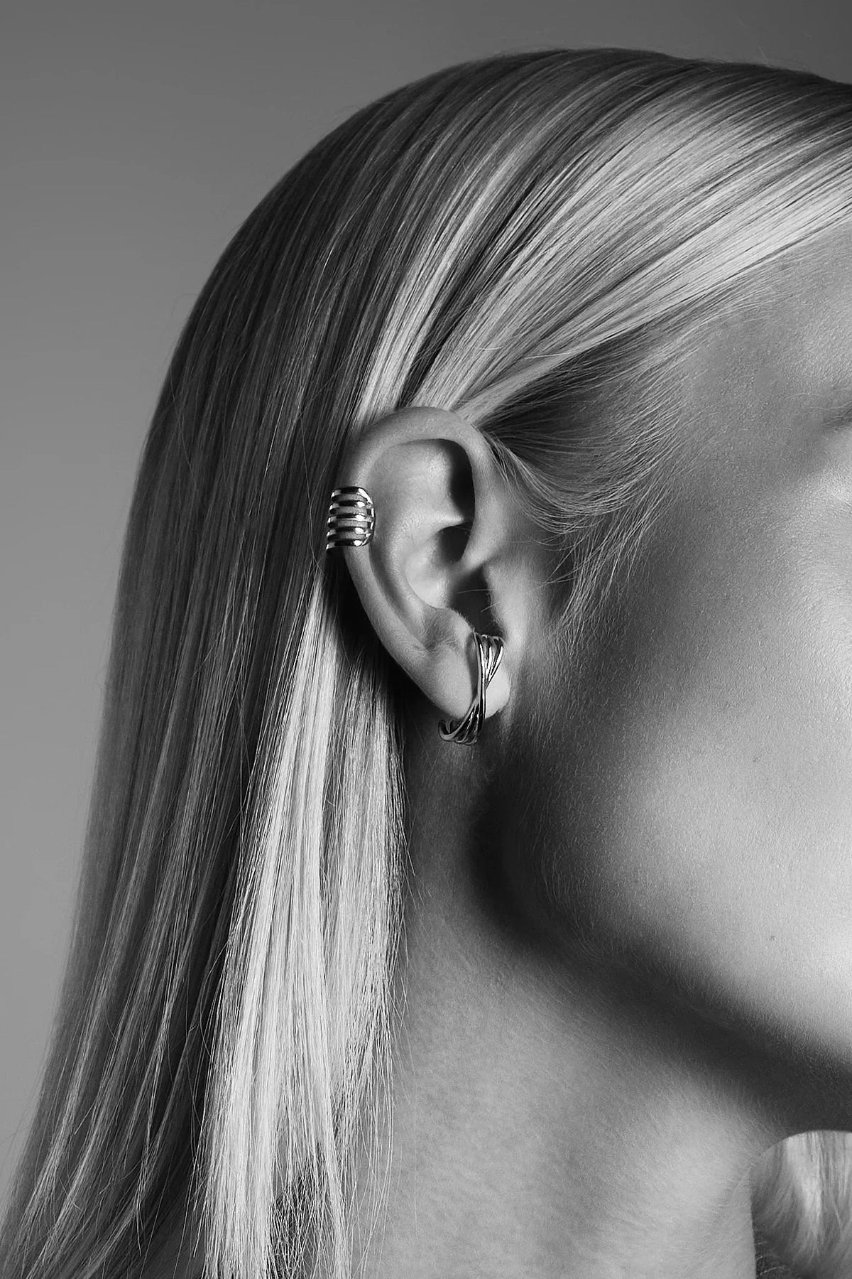 Close-up of a woman's ear with silver ear cuff and twisted hoop earring, minimal style