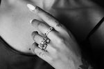 Close-up of hand with silver rings spelling DAD, BRO, MOM, and finger tattoos, on bare chest