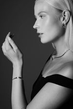 Woman wearing elegant silver necklace, hoop earrings, and bracelet in profile