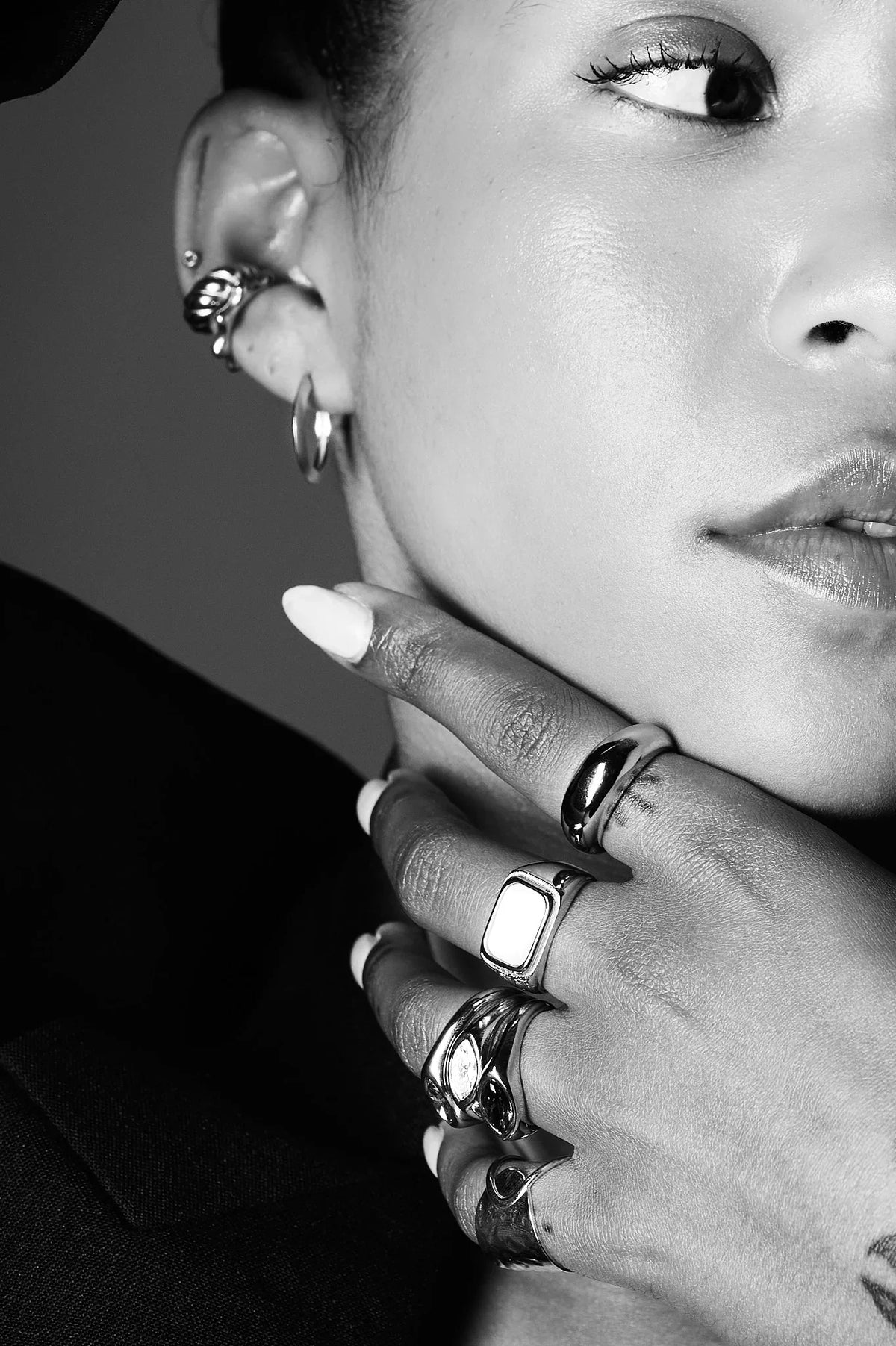 Close-up of woman wearing multiple statement rings and ear cuffs, monochrome jewellery shot