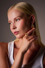 Woman wearing chunky gold statement ring and matching sculptural gold earrings
