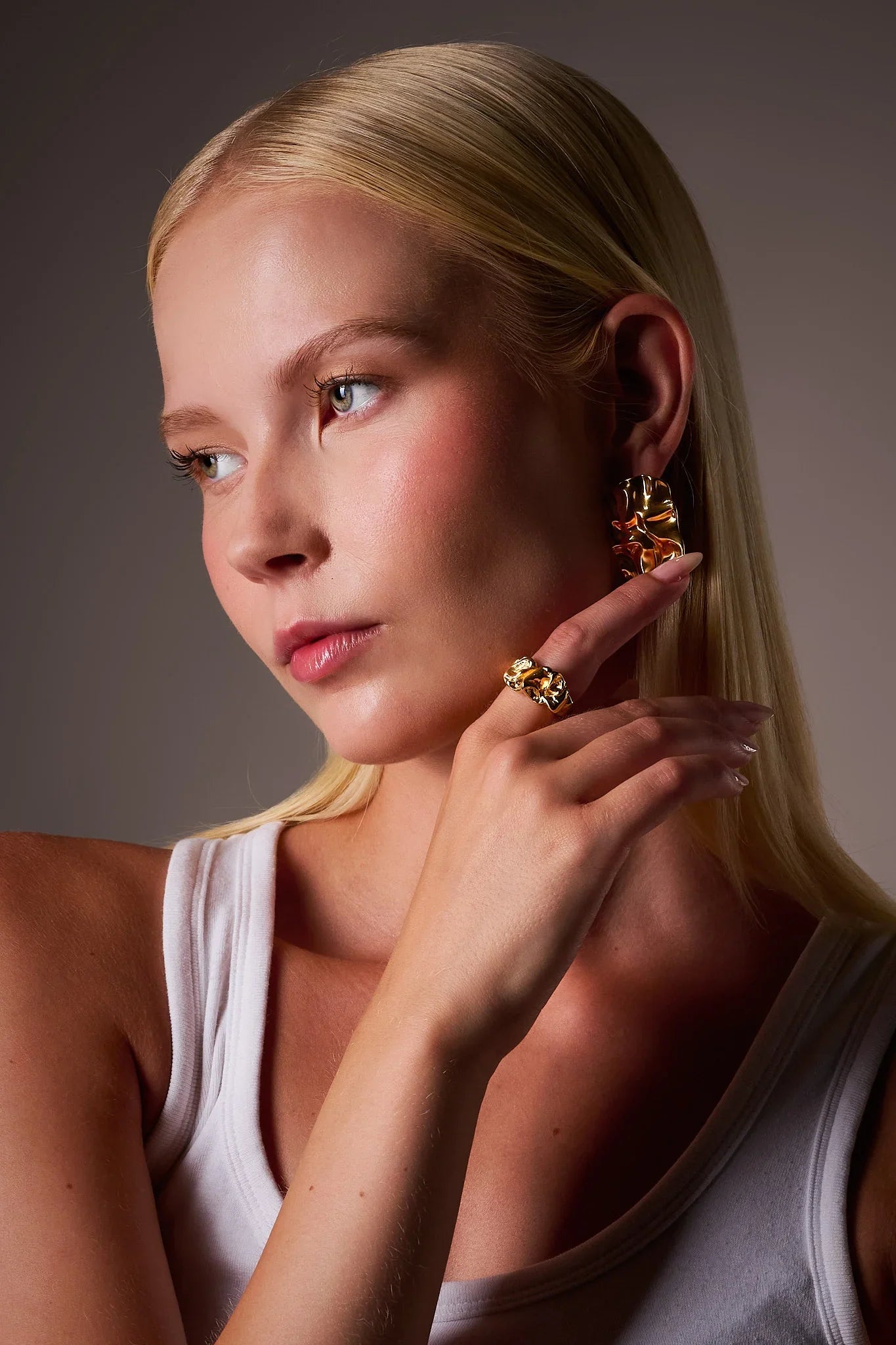 Woman wearing chunky gold statement ring and matching sculptural gold earrings