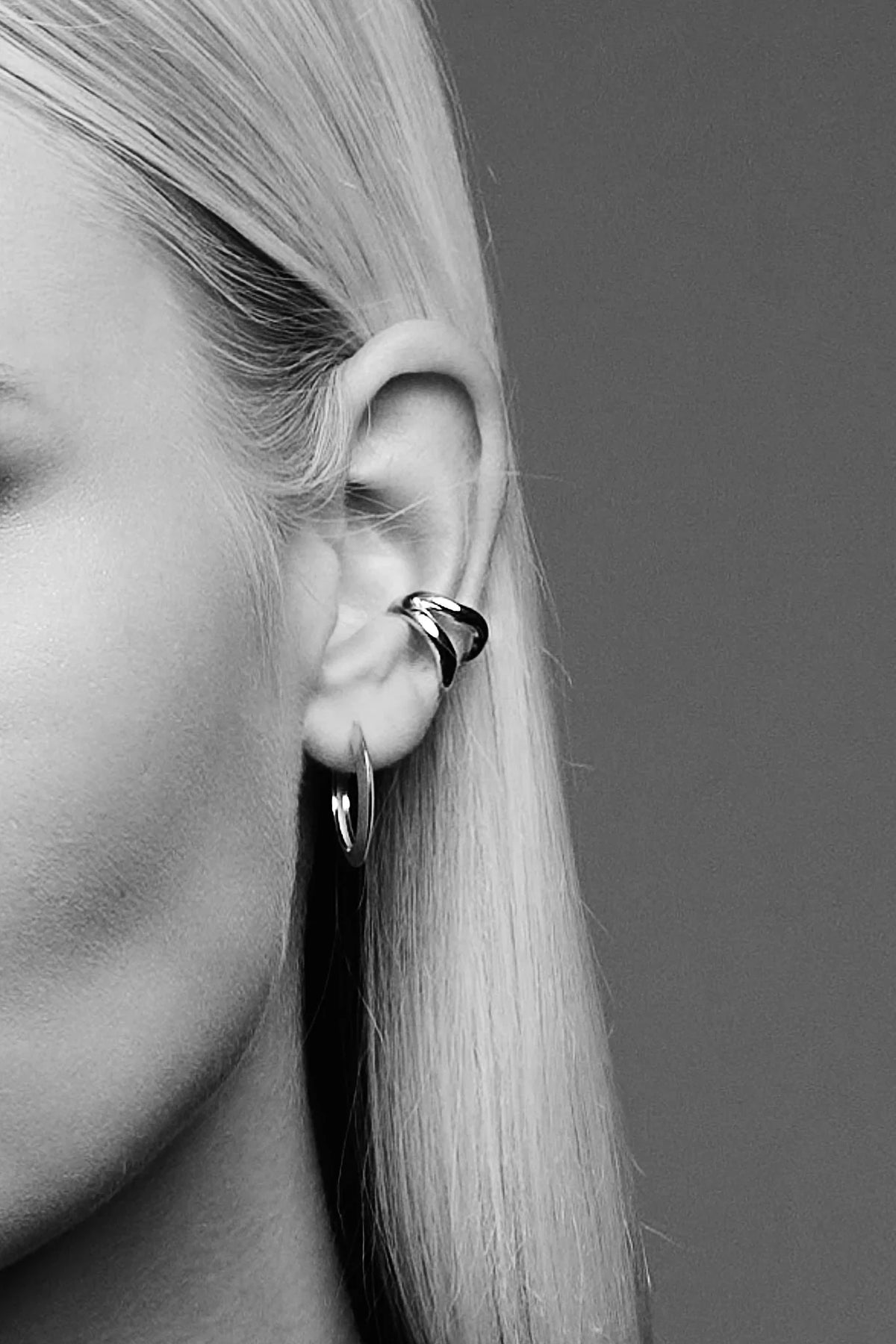 Close-up of woman's ear wearing modern silver hoop and ear cuff earrings