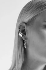 Close-up of a woman's ear wearing multiple silver earrings and ear cuffs, minimal style