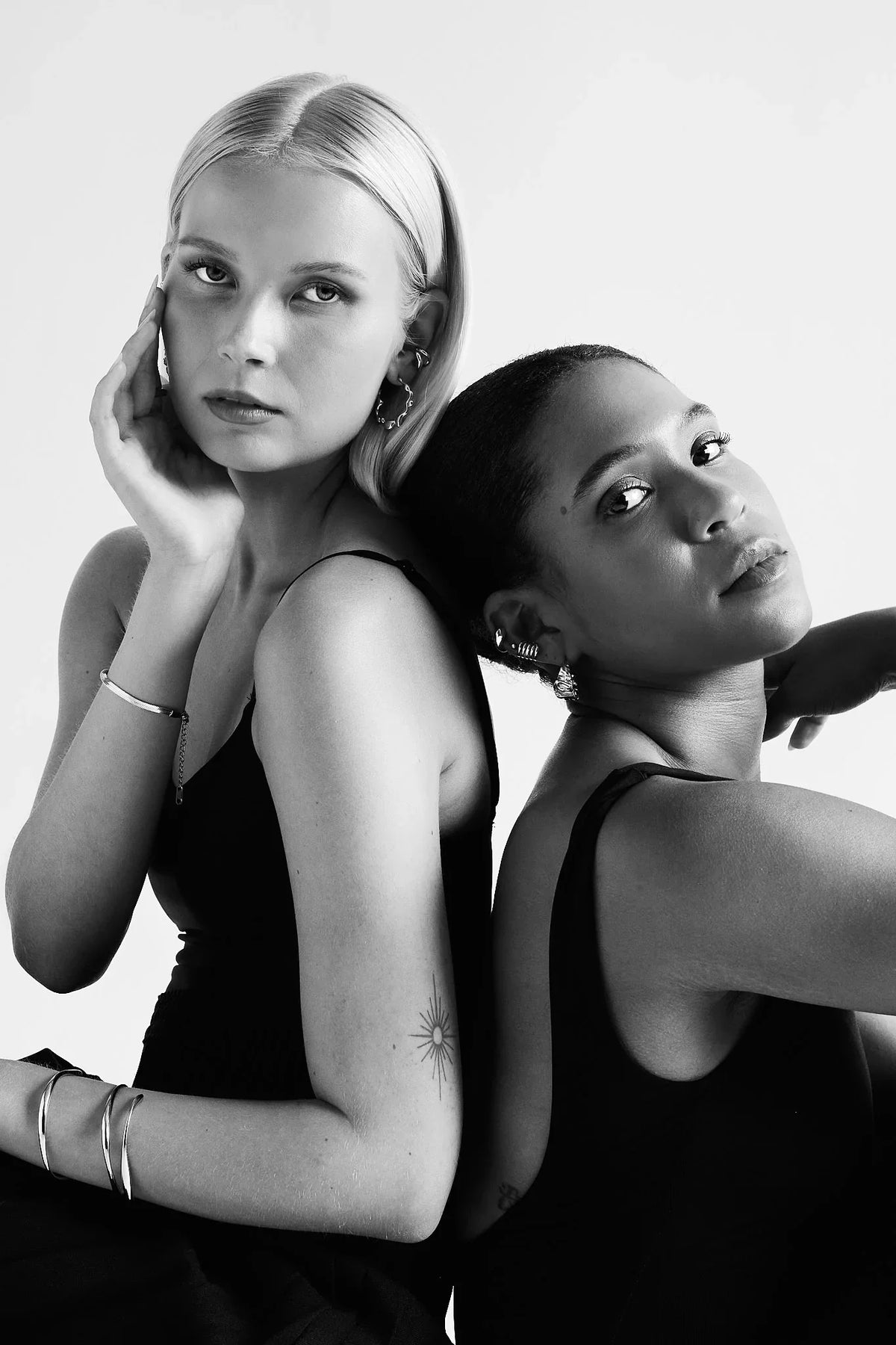 Two women in black clothing wearing modern silver earrings and bracelets, studio portrait