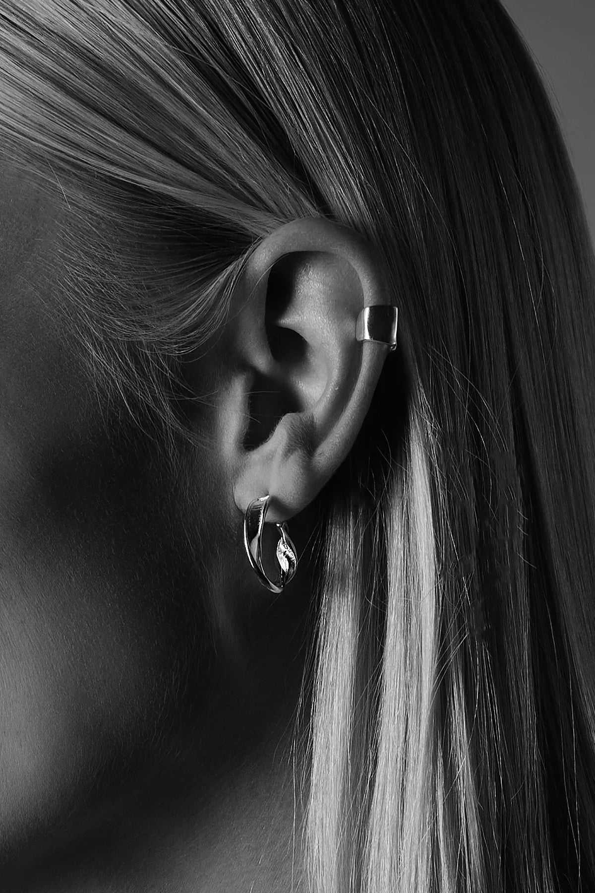 Close-up of a woman's ear with silver hoop earrings and a minimalist ear cuff