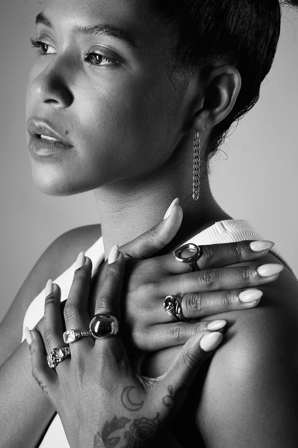Woman wearing statement rings and a chain drop earring, black and white close-up