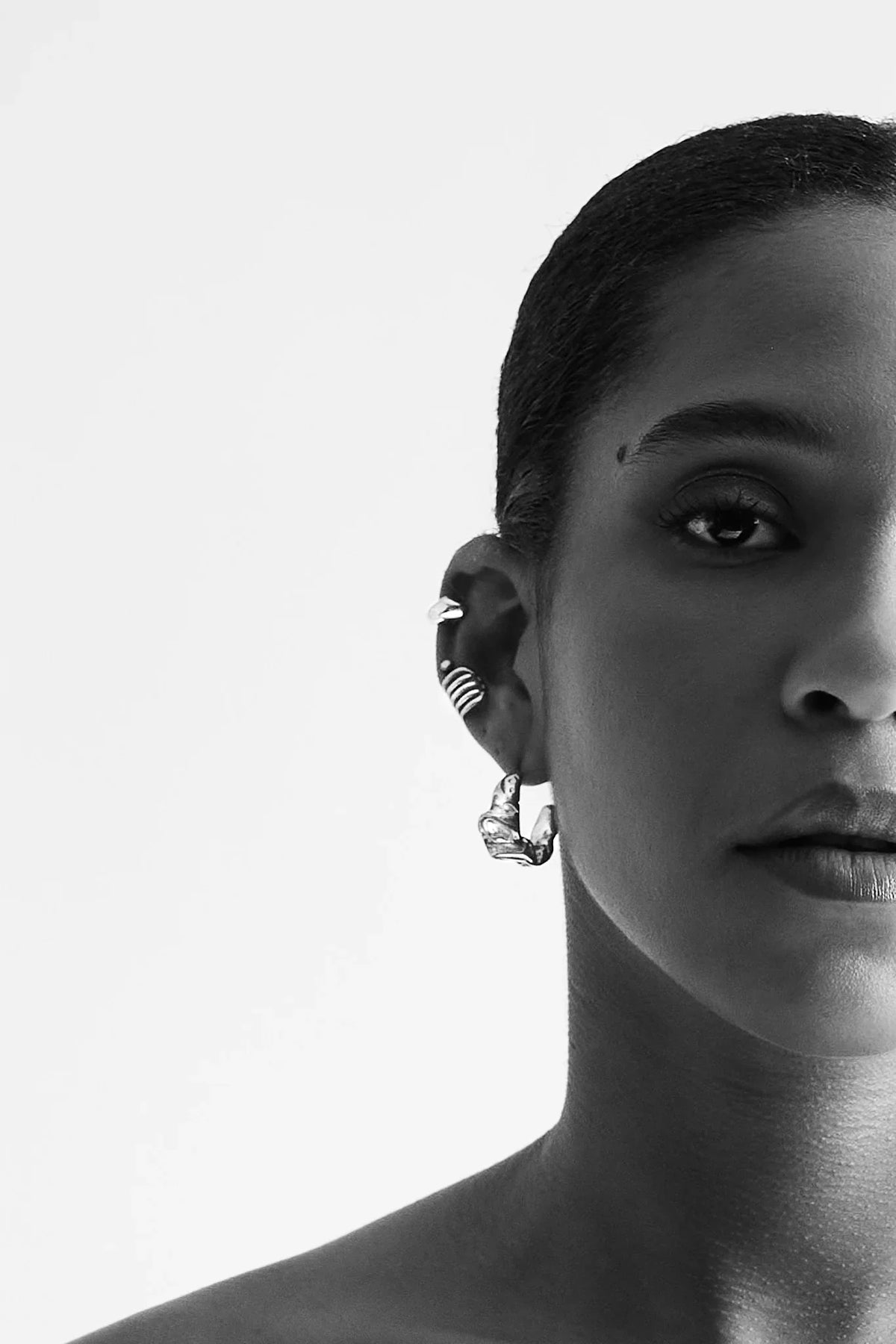 Close-up of woman wearing multiple silver statement earrings on ear, minimalist style