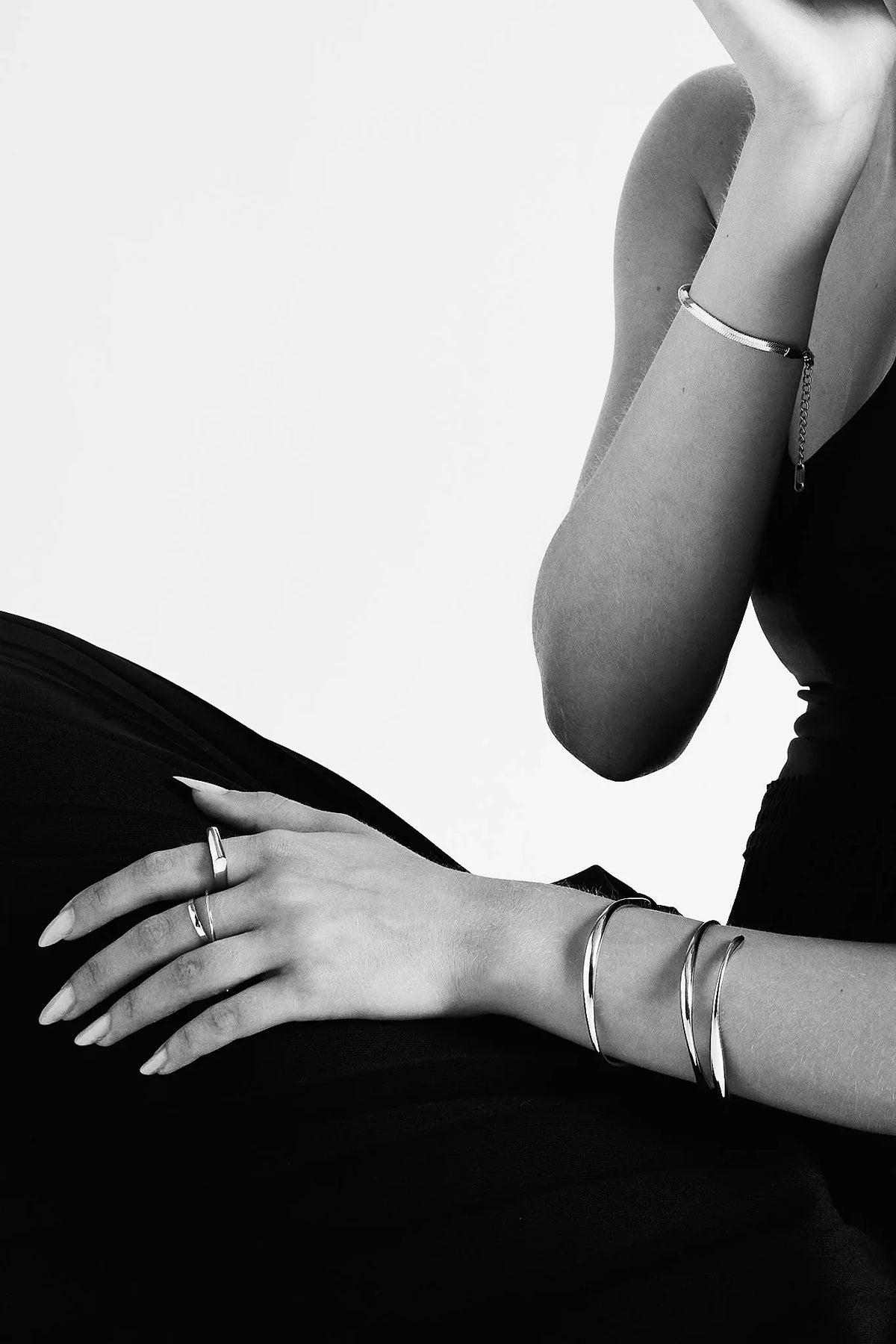 Woman wearing minimalist silver rings and bangles on wrist, black and white fashion shot