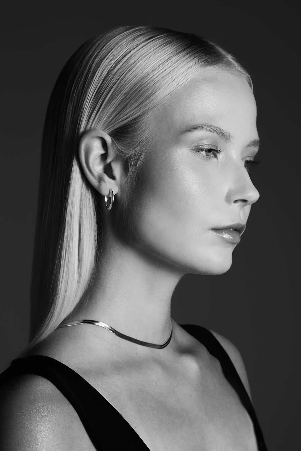 Woman wearing minimalist silver hoop earring and sleek chain necklace, side profile