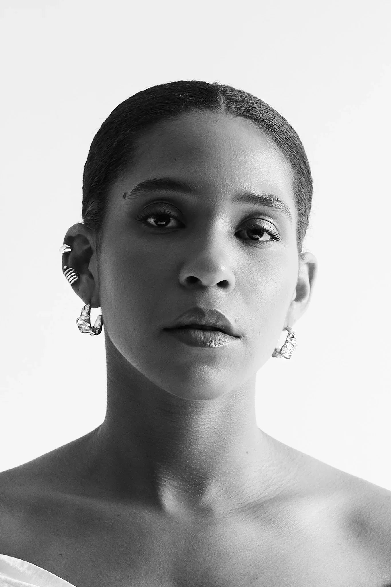 Woman wearing modern silver earrings and ear cuff, minimal black and white portrait