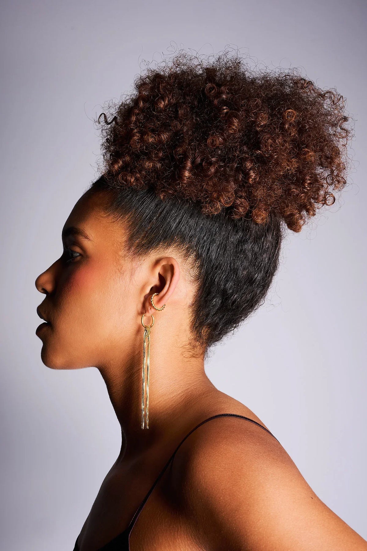 Woman wearing long gold chain drop earrings and gold hoop ear cuff, side profile view