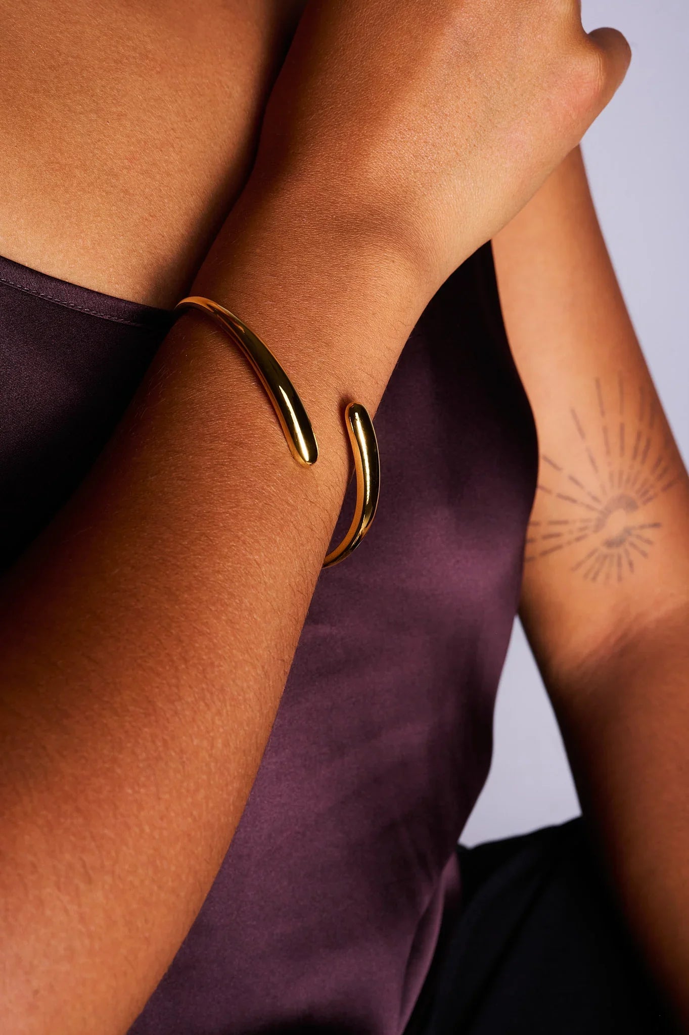 Minimalist gold open cuff bracelet on a woman's wrist with a sun ray tattoo