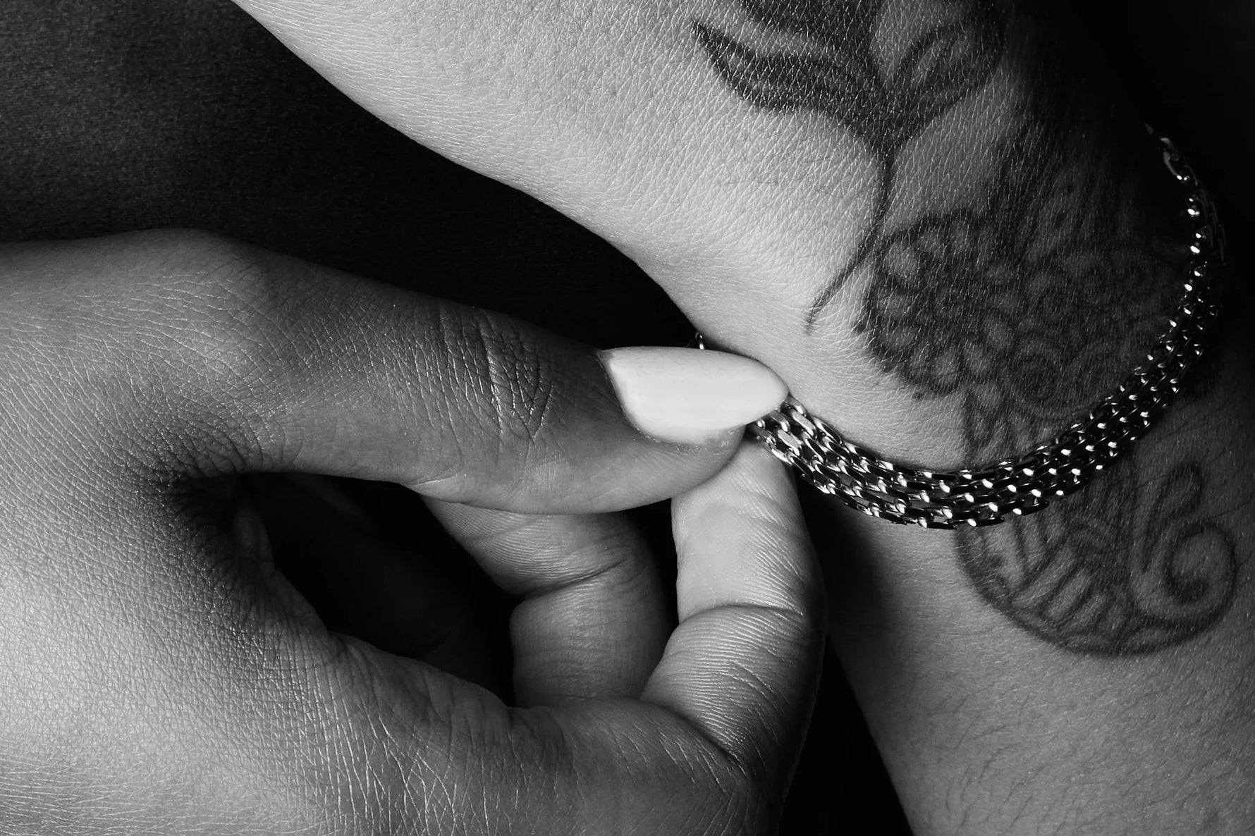 Close-up of a silver chain bracelet on a tattooed wrist, hand fastening jewelry.