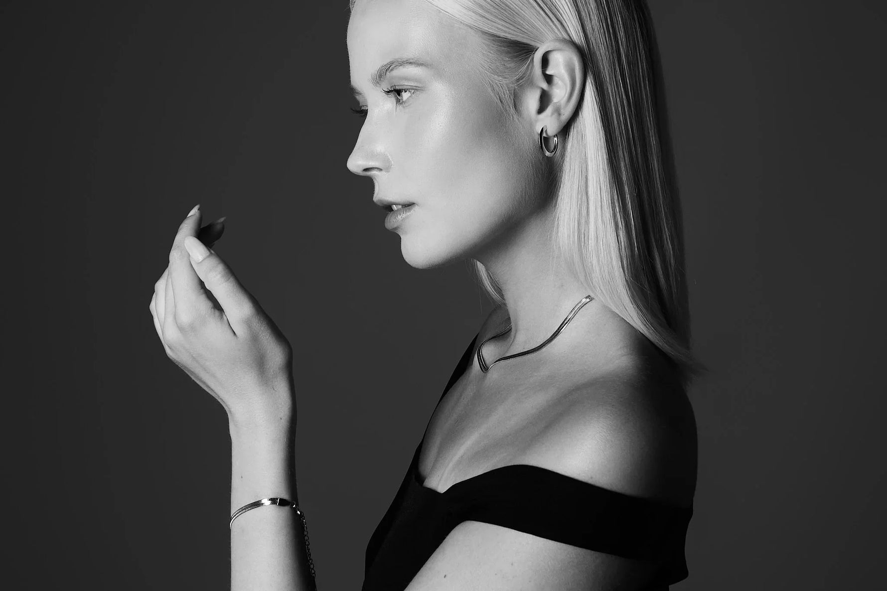 Woman wearing minimalist silver jewelry, including hoop earrings, necklace, and bracelet