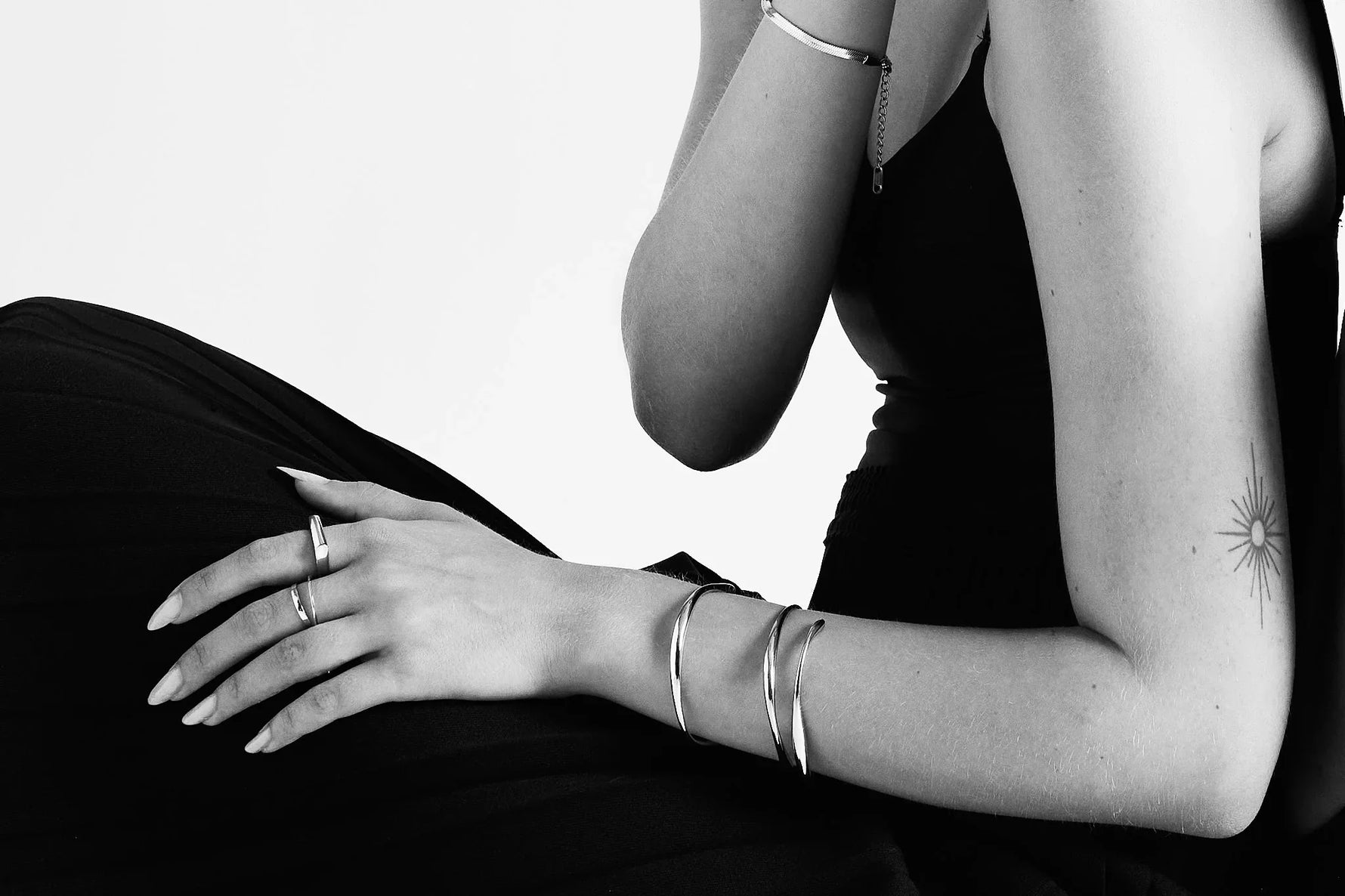 Woman wearing silver rings and bangles on arm, seated in black dress, minimal tattoo visible