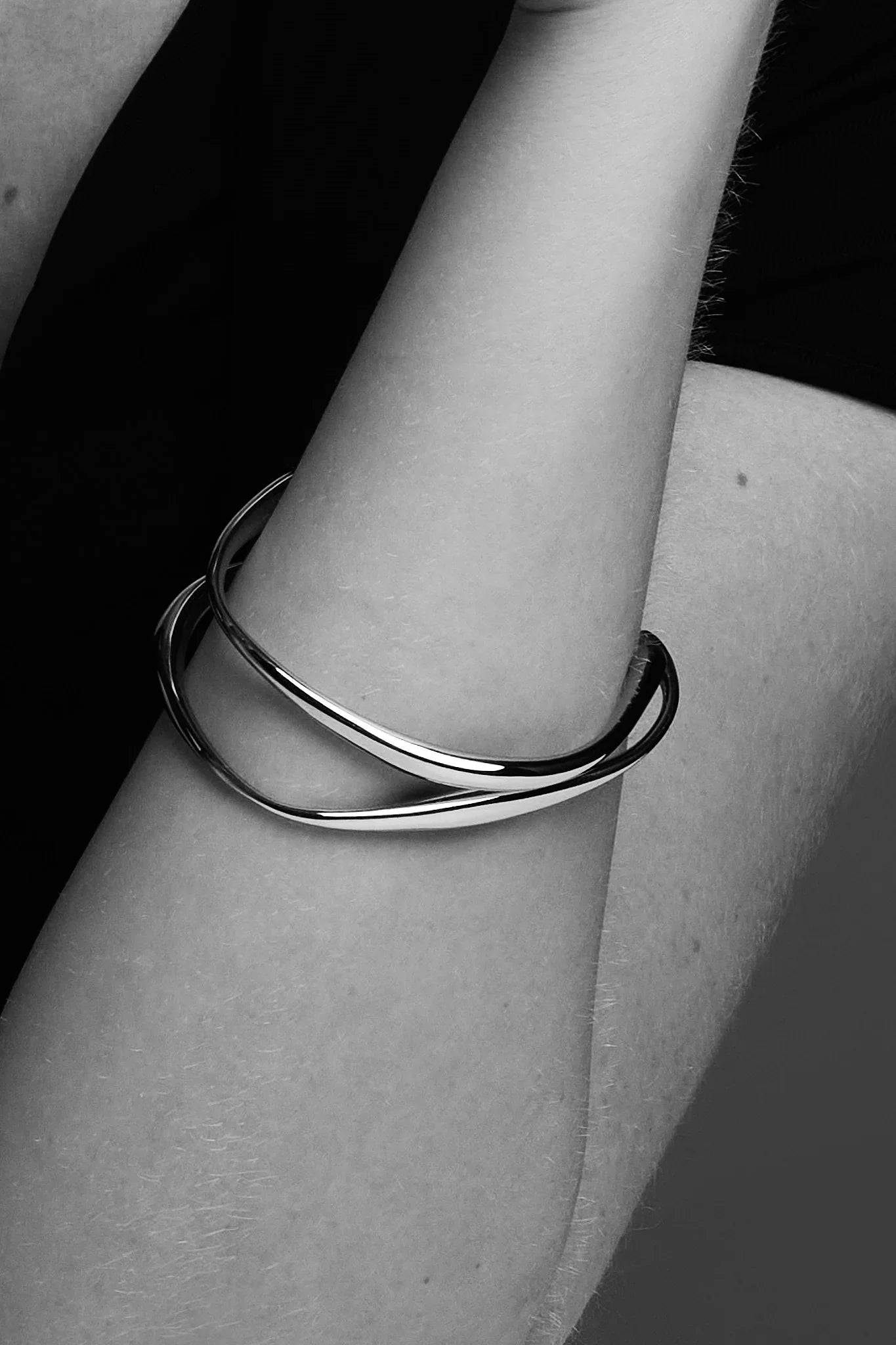 Minimalist silver bangle bracelet on a person's forearm, black background