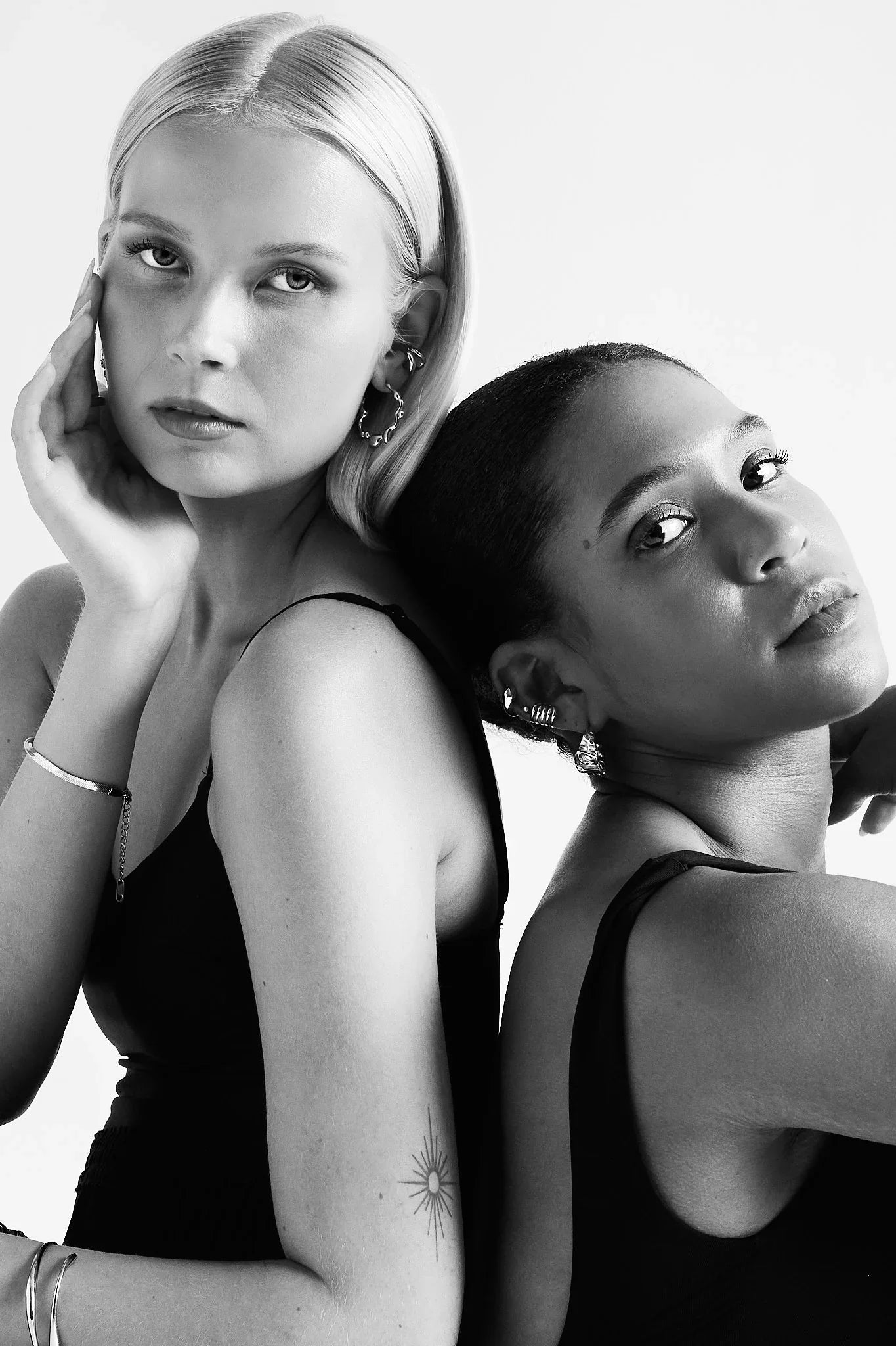 Two women wearing modern earrings, bracelets, and ear cuffs, posing in black tops