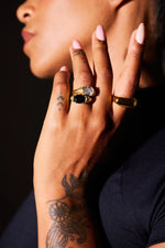 Close-up of hand with gold rings and gemstones, detailed floral tattoo on wrist.