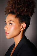 Woman wearing gold hoop earrings and a gold necklace, side profile, studio lighting