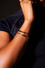 Close-up of arm wearing minimalist gold and silver bangles and gold rings, black shirt background