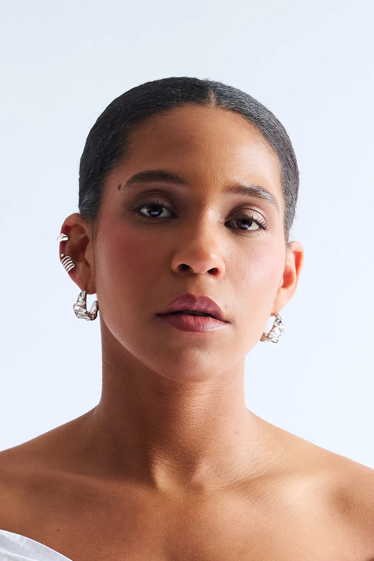 Woman wearing sculptural silver hoop earrings and ear cuffs against white background