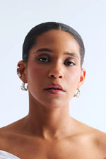 Woman wearing sculptural silver hoop earrings and ear cuffs against white background