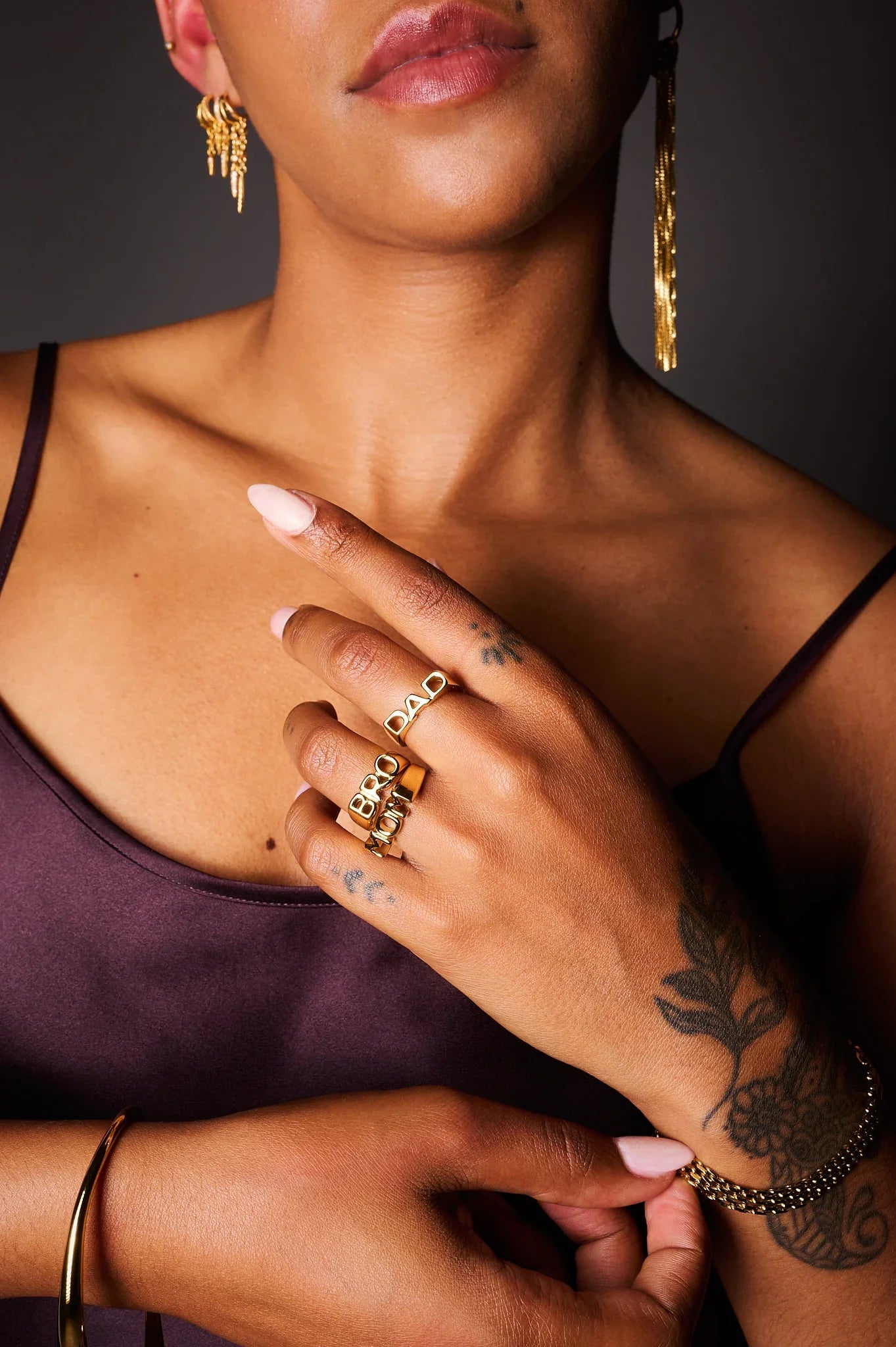 Woman wearing gold jewelry rings with letter engravings, gold bracelet, and long earrings