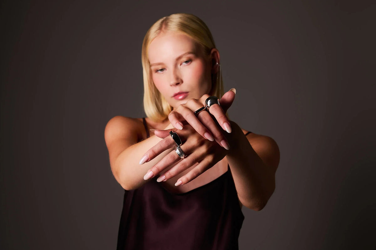 Woman wearing bold silver rings on both hands, showing jewelry against a dark background