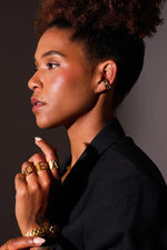 Woman wearing gold jewelry, including chunky letter rings and hoop earrings, in profile
