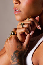 Close-up of a woman wearing gold rings with gemstone details and visible hand tattoo