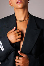 Woman wearing gold chunky chain necklace, gold rings, earrings, and black blazer