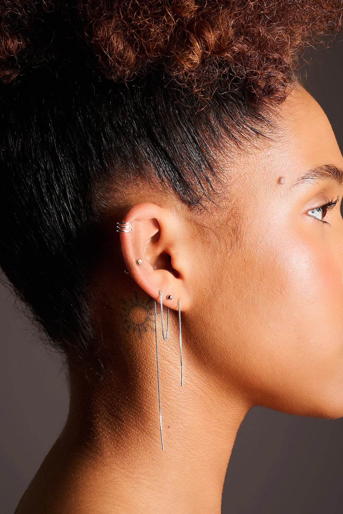 Woman wearing multiple silver earrings, ear cuffs, and long threader earring on left ear