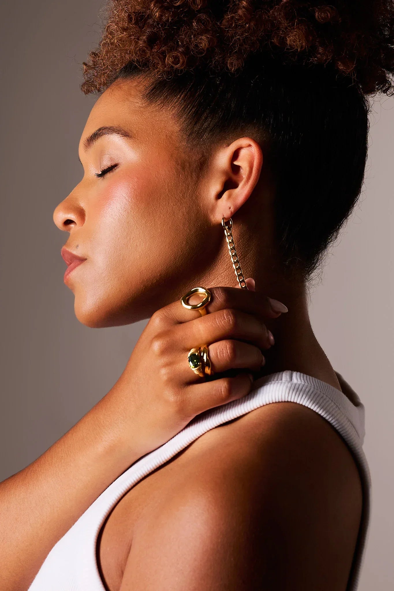 Woman wearing gold chain earring and gold rings with gemstone, white tank top