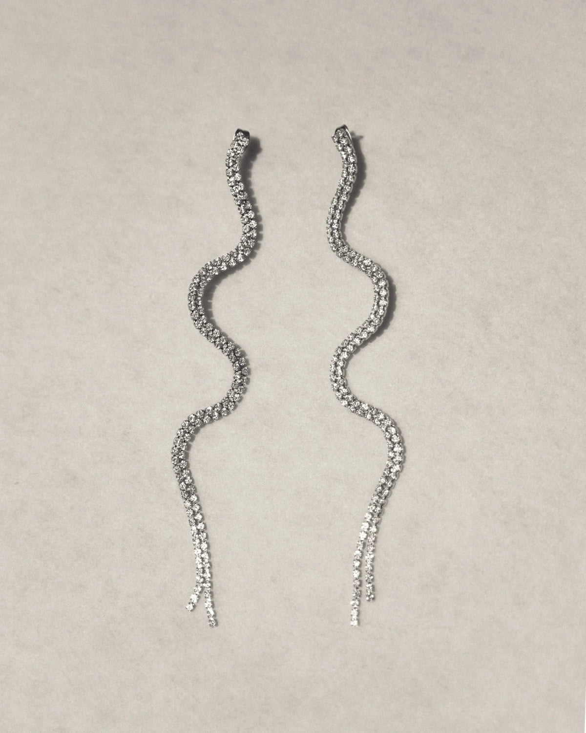 Wavy silver drop earrings with sparkling crystals on a light background