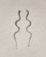 Wavy silver drop earrings with sparkling crystals on a light background