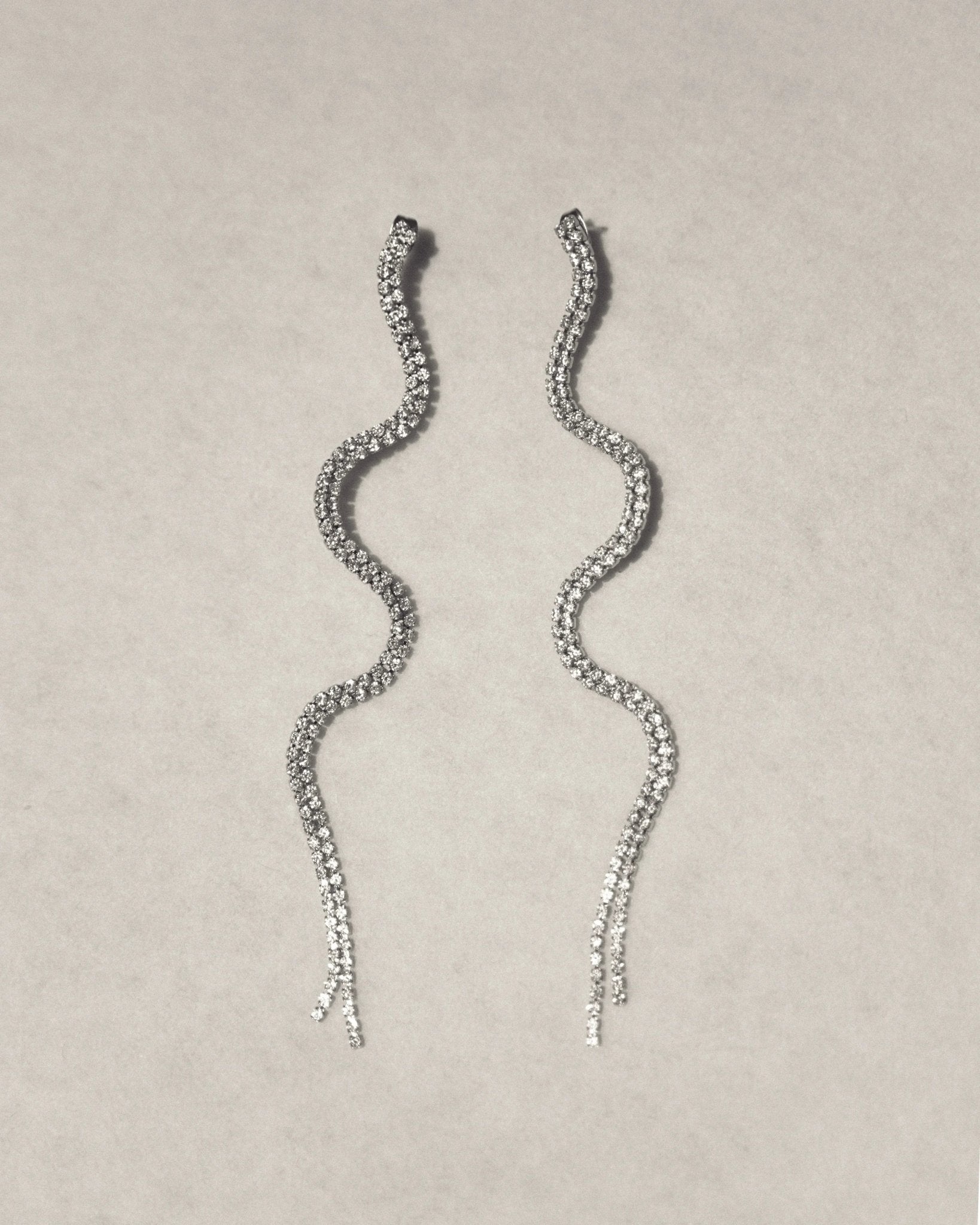 Wavy silver drop earrings with sparkling crystals on a light background