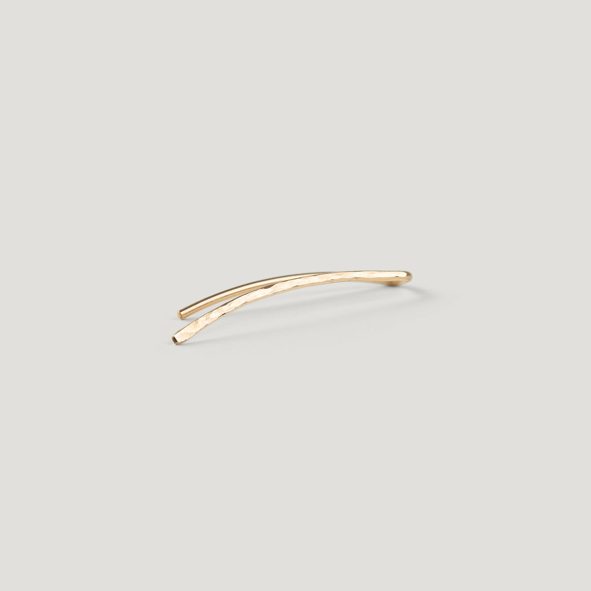Single gold curved bar ear climber with a hammered texture, close-up on light background.