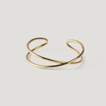 Gold cuff bangle with a crossed double-band design, laid flat on light background.