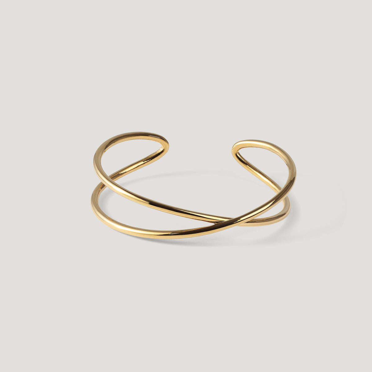 Gold cuff bangle with a crossed double-band design, laid flat on light background.