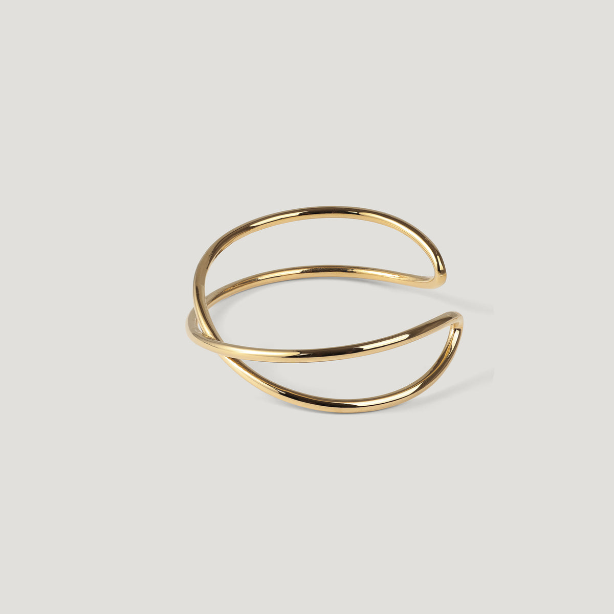 Gold crossed cuff bangle standing upright at an angle, on light background.