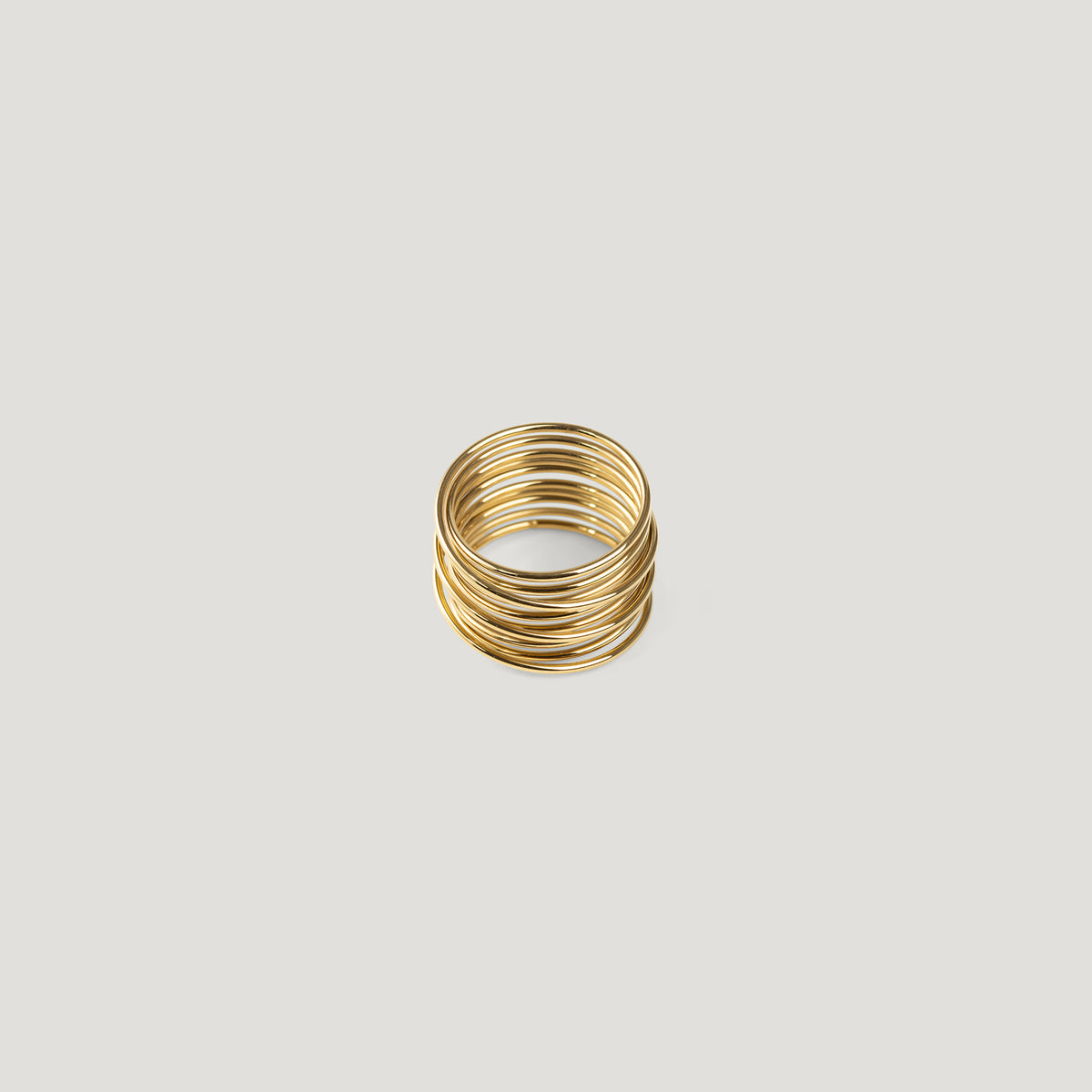 Gold statement ring made of tightly stacked wire coils, front view on light background.